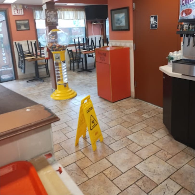 Interior of Jersey Johnny's Grill with stacked chairs, a gumball machine, and a wet floor sign.