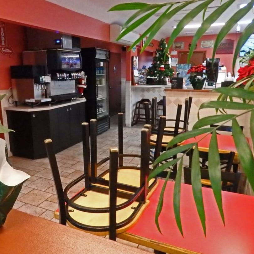Interior of Jersey Johnny's Grill with red walls, soda machines, and chairs stacked on tables.