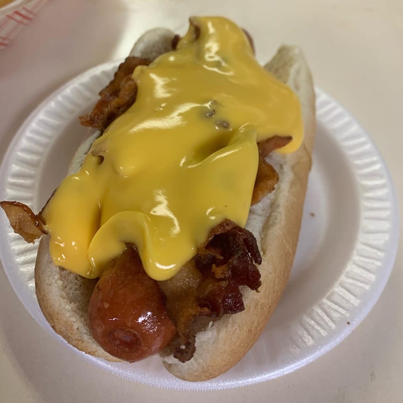 A Jersey Johnny's Grill hot dog with melted cheese and bacon on a white paper plate.