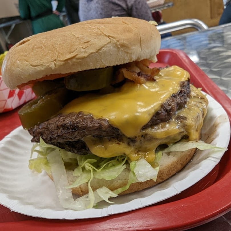 A double cheeseburger with melted cheese, pickles, and lettuce on a bun, served on a red tray.